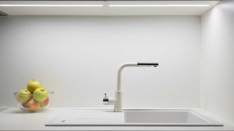 Biely kuchynský drez vedľa varnej dosky s LED podsvietením zospodu vrchných skriniek