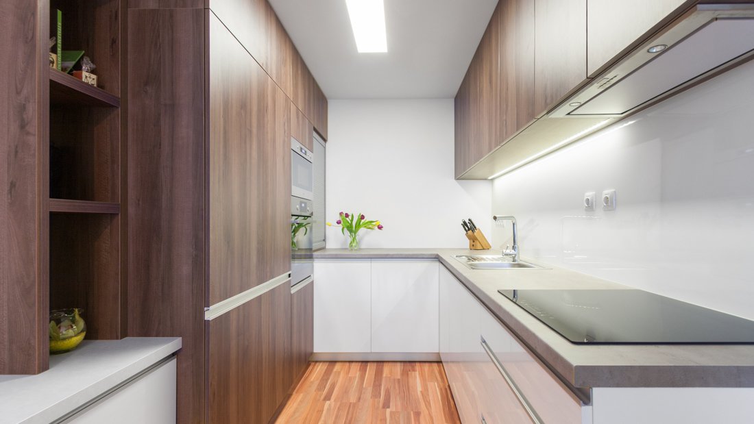 Moderná úzka kuchyňa tvaru U v paneláku s farebnou kombináciou bielej a dreva s malou knižnicou na mieru