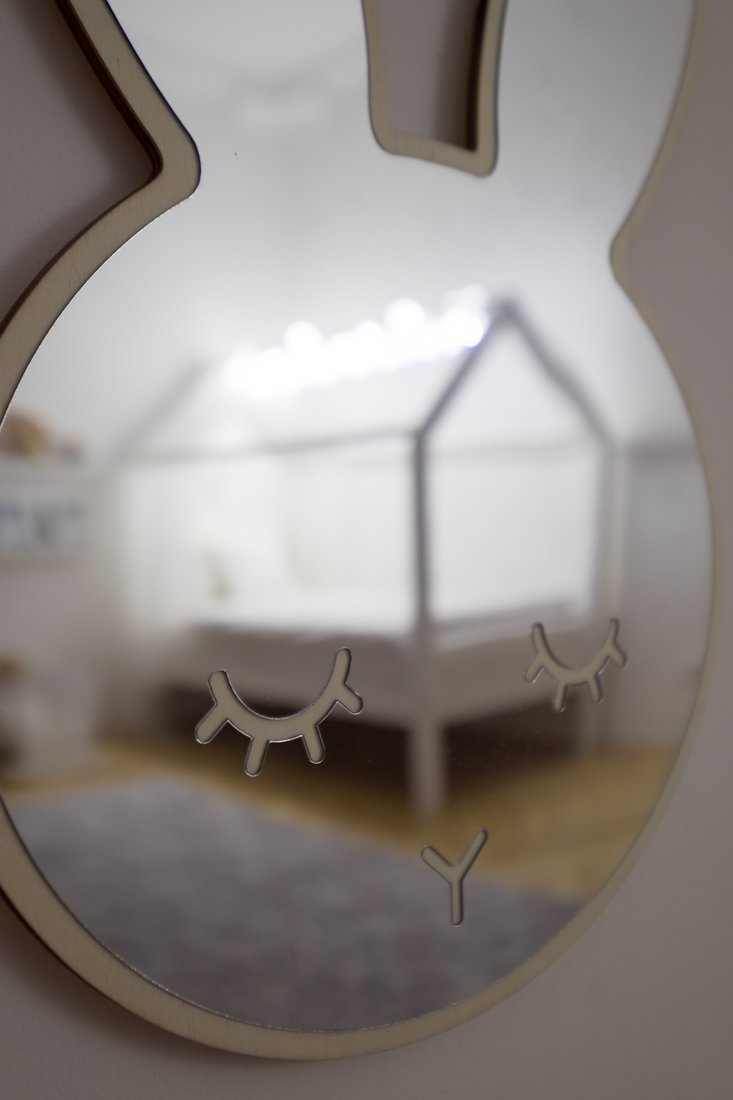 Detské zrkadlo tvaru zajačej hlavy ukazujúce roh izby s kobercom a osvetlenou posteľou s výzorom domčeka