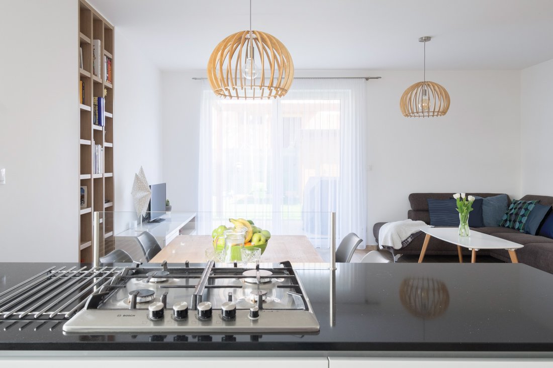 Kuchyňa s obývačkou a jedálenským stolom vo farebnej kombinácii bielej a bledého dreva s občasnými tmavými elementami