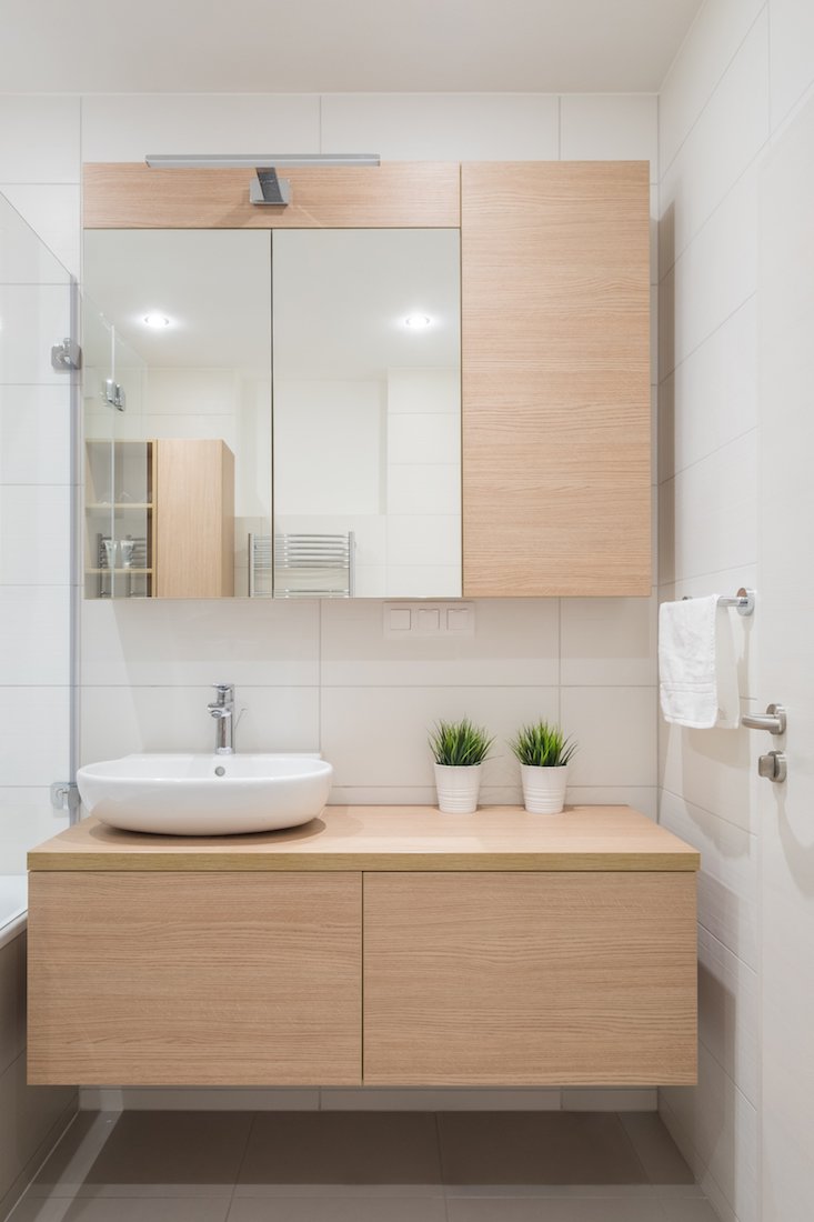 Drevená skrinka so zrkadlom v bielej kúpeľni s vaňou