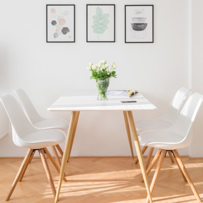 Biely jedálenský stôl so štyrmi stoličkami v rovnakom škandinávskom štýle pod troma menšími obrazmi