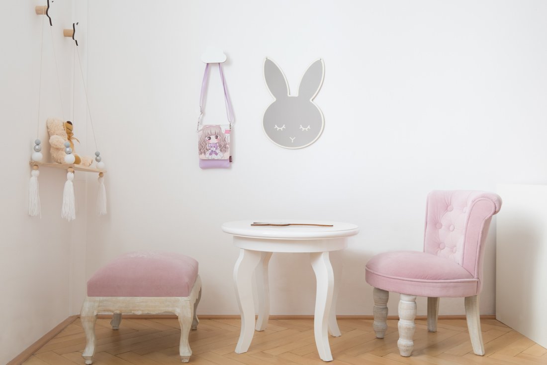 Kútik v detskej izbe s malým nábytkom pod zrkadlom tvaru zajačej hlavy a vešiakmi pre hračky na stene