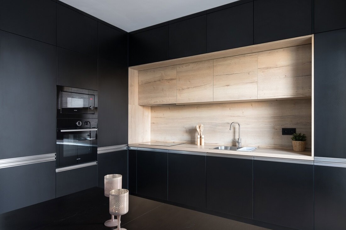 Roh kuchyne s čiernou kuchynskou linkou tvaru L a kontrastným dreveným dekórom oproti čiernemu kuchynskému stolu
