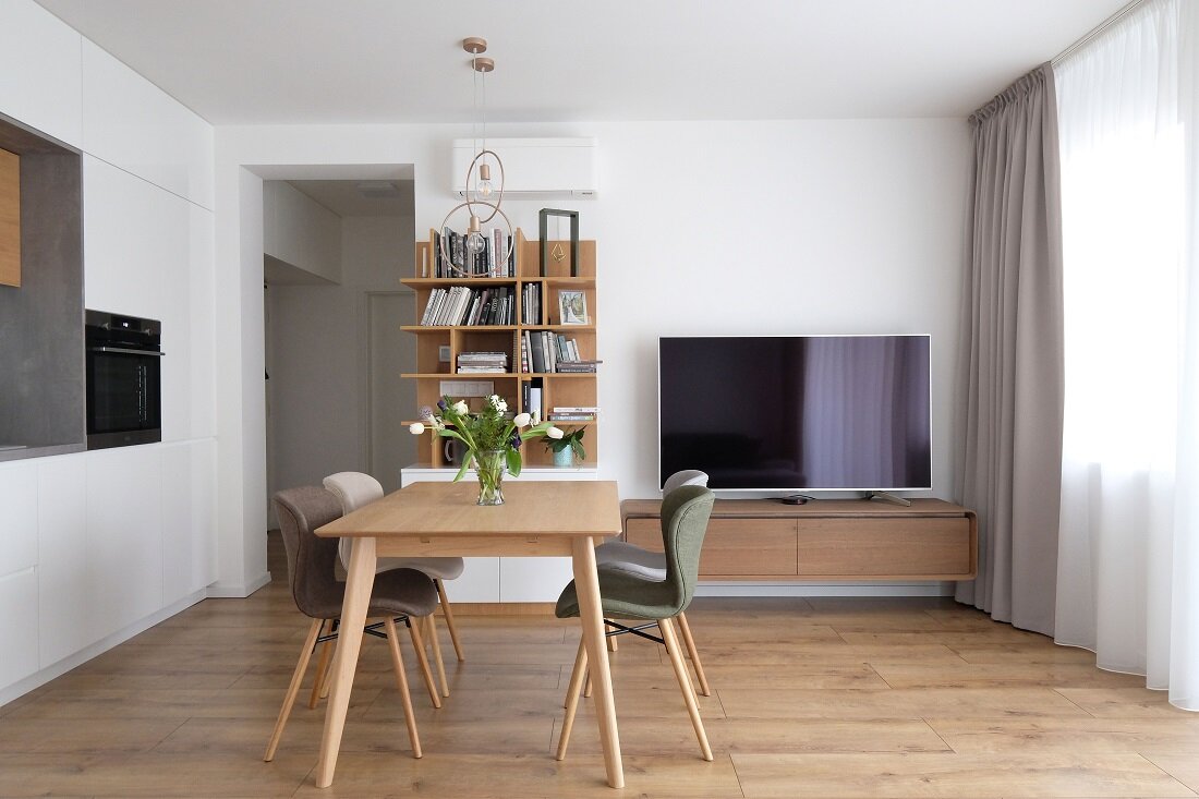 Priestranná kuchyňa s obývačkou, knižnicou a jedálenským stolom v kombinácii bielej a dreva až na rôznofarebné stoličky