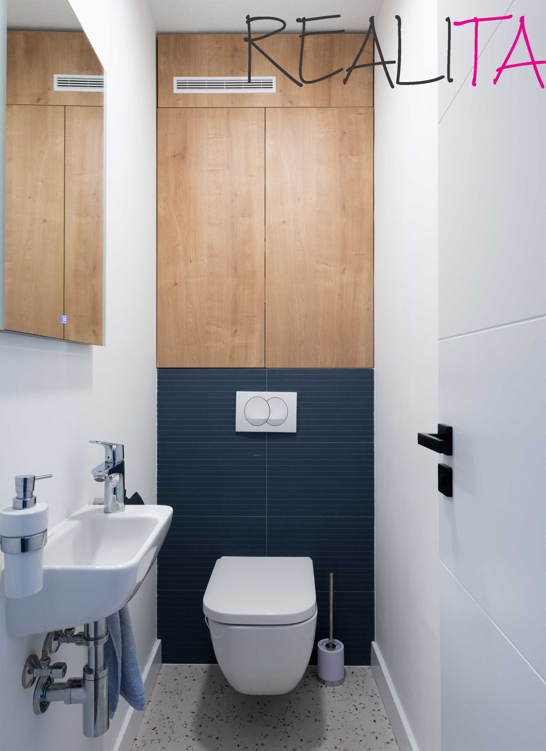 Záchod s umývadlom a zrkadlom, spestrený tmavomodrým obkladom a drevenou skrinkou na jednej stene